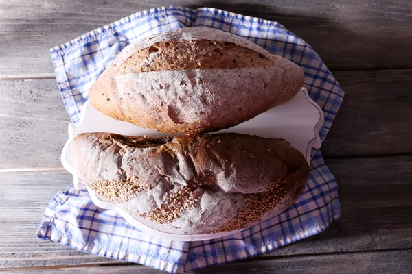 Pão caseiro fresco embrulhado em papel, em guardanapo, na cor de fundo de madeira — Fotografia de Stock