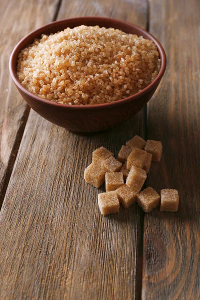 Кубики коричневого сахара и хрустальный сахар в миске на деревянном фоне — стоковое фото