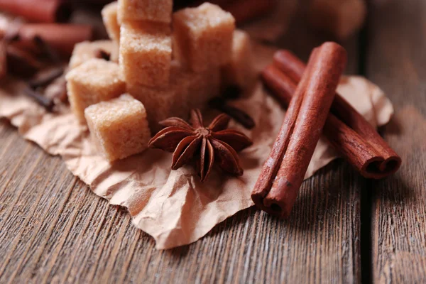 Cubos de açúcar mascavo na tigela, anis estrelado e paus de canela no fundo de madeira — Fotografia de Stock