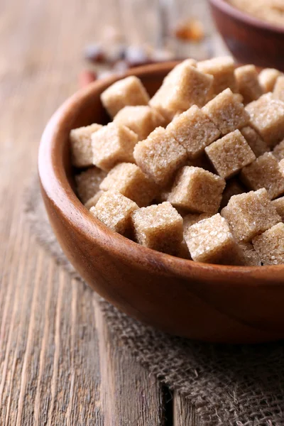 Braune Zuckerwürfel, Schilf und Kristallzucker in Schüssel auf Holzgrund — Stockfoto