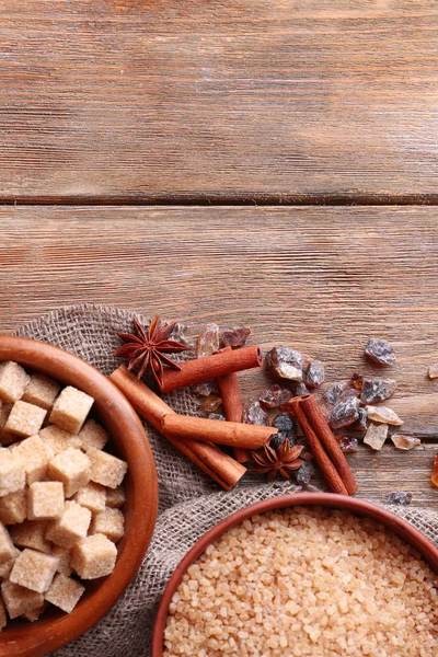 Кубики коричневого сахара, камыш и хрустальный сахар в миске со специями на деревянном фоне — стоковое фото