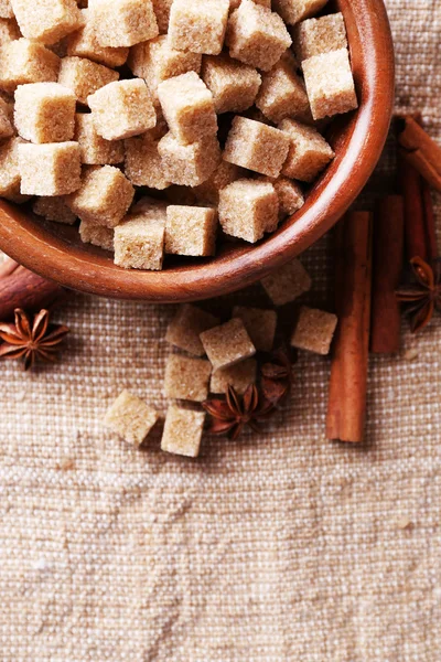 Brown sugar cubes and crystal sugar, spices in bowl on sackcloth background — Stock Photo, Image