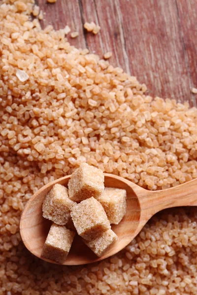 Brown sugar cubes in wooden spoon on crystal sugar background — Stock Photo, Image