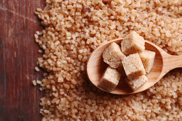 Kostki cukru brązowego w drewnianą łyżką na tle cukru kryształu — Zdjęcie stockowe