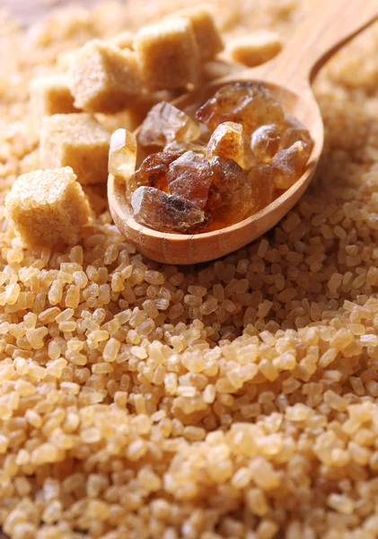 Reed sugar in wooden spoon on brown crystal sugar background — Stock Photo, Image