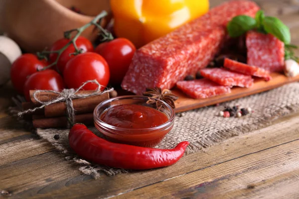 Leckere Salamiwurst und Gewürze auf Holzgrund — Stockfoto