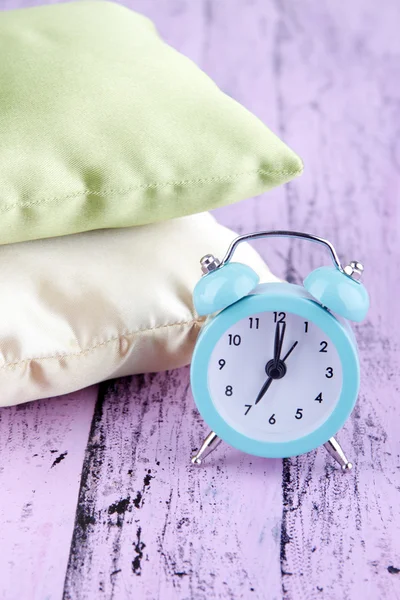 Plastic clock on a silk pillows on wooden purple background — Stock Photo, Image