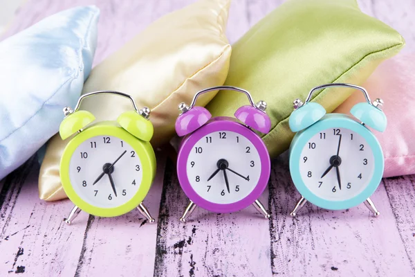 Plastic clocks on a silk pillows on wooden background — Stock Photo, Image