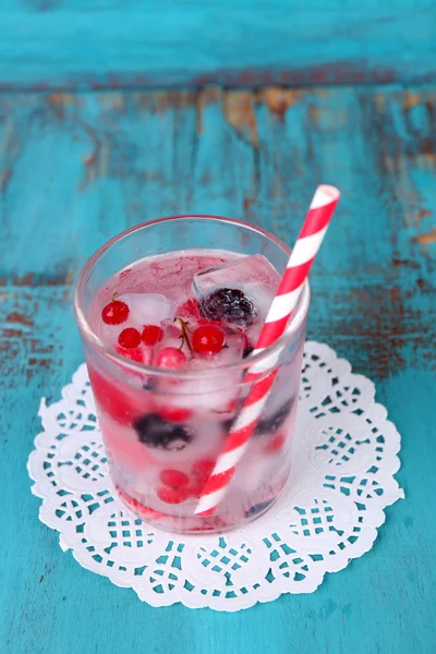 Cold cocktail with forest berries, frozen in ice cubes on color wooden background — Stock Photo, Image