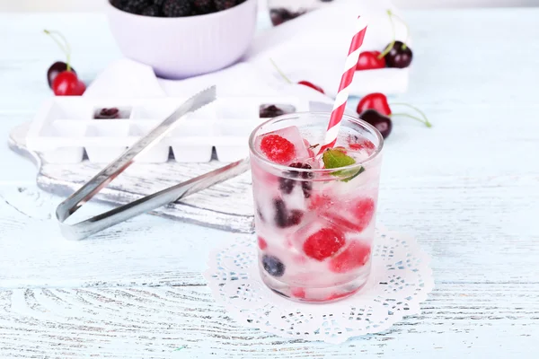 Cold cocktail with forest berries, frozen in ice cubes on wooden table background — Stock Photo, Image