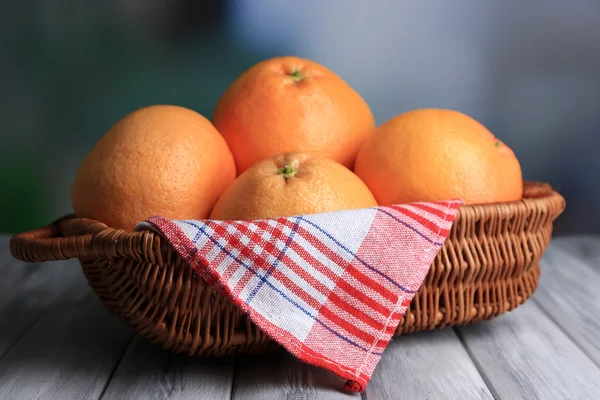 Ripe grapefruits in wicker basket on wooden table, on bright background — Stock Photo, Image