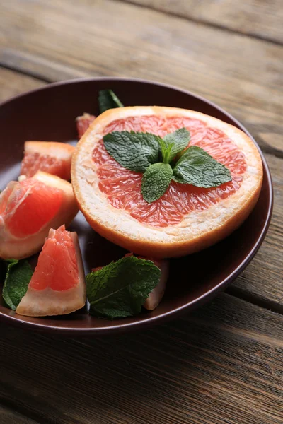 Ripe chopped grapefruit with mint leaves on plate, on wooden background — Stock Photo, Image