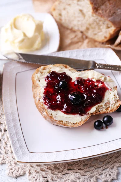 Fresh bread with homemade butter and blackcurrant jam on plate, on light wooden background — Stock Photo, Image