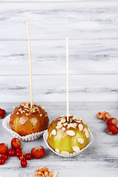 Sweet caramel apples on sticks with berries, on wooden table — Stock Photo, Image