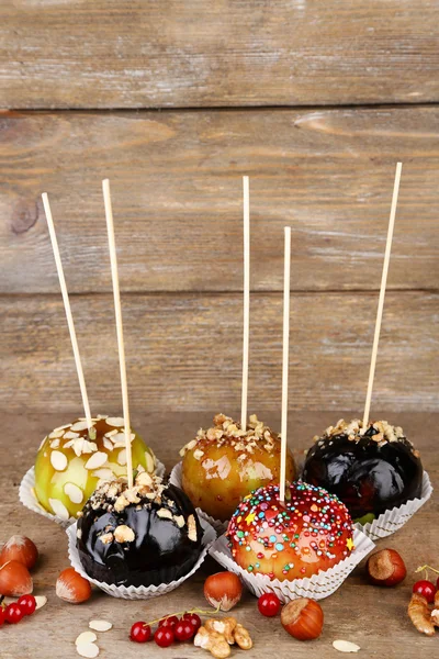 Sweet caramel apples on sticks with berries, on wooden table — Stock Photo, Image