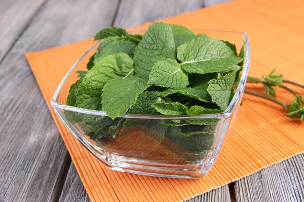 Glazen vierkante kom van mint verlaat op een oranje servet op houten achtergrond — Stockfoto