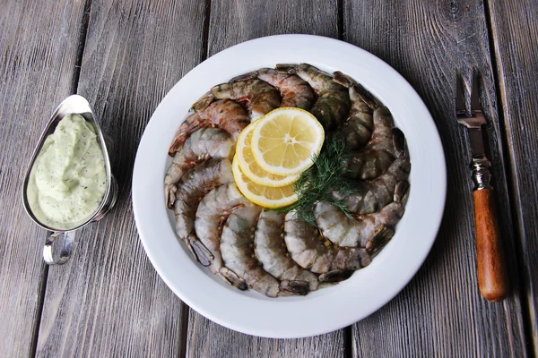 Plato redondo blanco de langostinos con eneldo, limón y salsa sobre una servilleta amarilla sobre fondo de madera gris — Foto de Stock