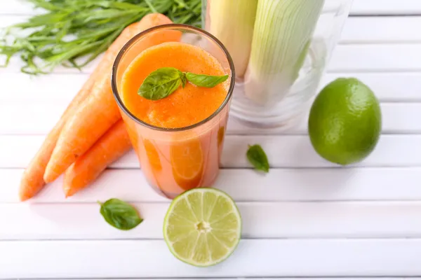 Verre de jus de carotte frais, oignon de printemps, citron vert, touffe d'herbe et de carotte sur fond en bois — Photo