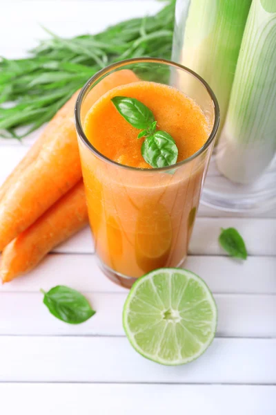 Bicchiere di succo di carota fresco, cipollotto, lime, ciuffo d'erba e carota su fondo di legno — Foto Stock