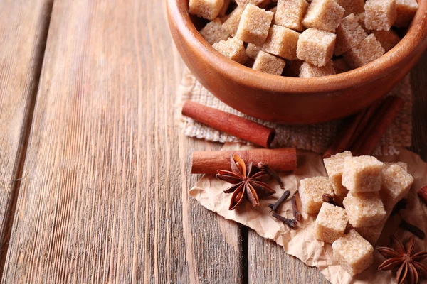 Zucchero di canna cubetti in ciotola, anice stellato e cannella bastoncini su sfondo di legno — Foto Stock