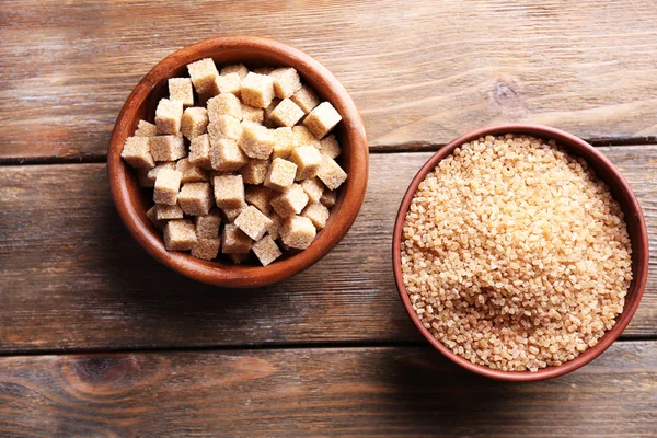 Cubos de azúcar moreno y azúcar de cristal en un tazón sobre fondo de madera — Foto de Stock