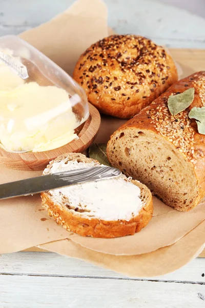 Baked bread and toast with fresh butter, on cutting board, on wooden background — Stock Photo, Image