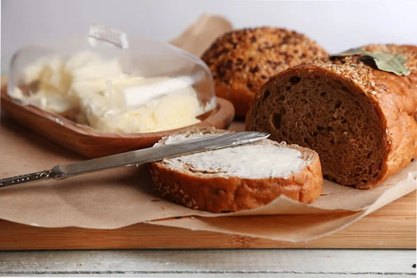 Pain cuit et pain grillé au beurre frais, sur planche à découper, sur fond de bois — Photo