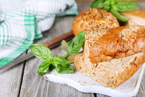 Свежий хлеб и свежий базилик на разделочной доске, на деревянном фоне
