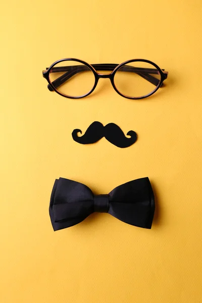 Glasses, mustache and bow tie forming man face on yellow background — Stock Photo, Image