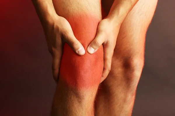 Πόνος concept.young άνθρωπος με πόνους στα γόνατα σε σκούρο φόντο — Φωτογραφία Αρχείου