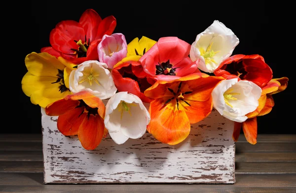 Hermosos tulipanes en cubo en caja de madera sobre mesa sobre fondo negro —  Fotos de Stock