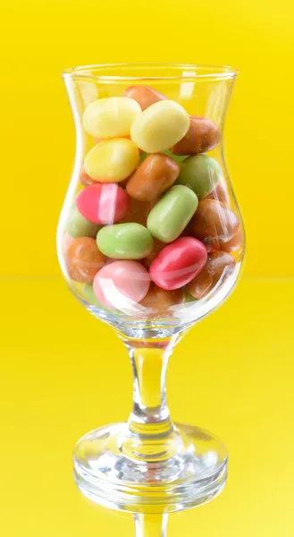 Verschiedene bunte Fruchtbonbons im Glas auf gelbem Hintergrund — Stockfoto