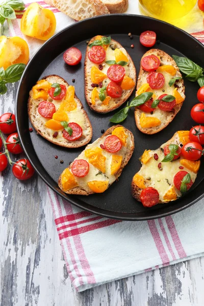 Chutné bruschetta s rajčaty na pánvi, na starý dřevěný stůl — Stock fotografie