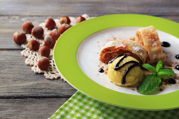 Leckerer hausgemachter Apfelstrudel mit Nüssen, Minzblättern und Eis auf Teller, auf Holzgrund — Stockfoto