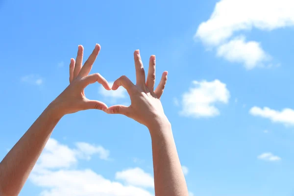 Menina jovem de mãos dadas em forma de coração enquadrando no fundo do céu azul — Fotografia de Stock