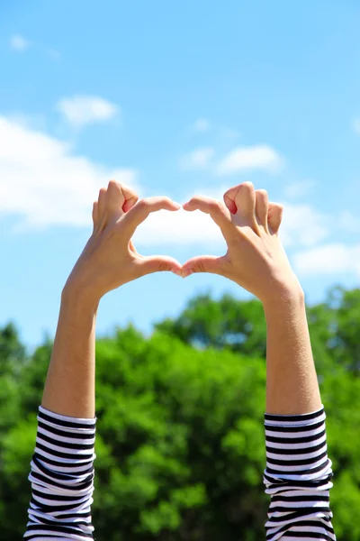 心臓形状フレーミングで青い空を背景に手を保持している若い女の子 — ストック写真