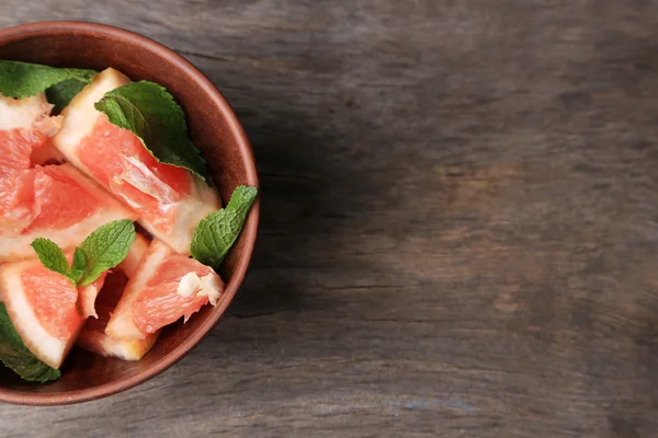 Ripe chopped grapefruit with mint leaves on plate, on wooden background — Stock Photo, Image