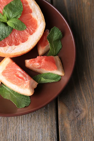 Спелый грейпфрут с мятными листьями на тарелке, на деревянном фоне — стоковое фото
