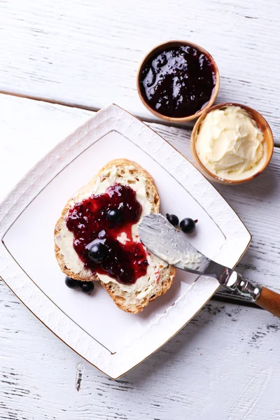 Pane fresco con burro fatto in casa e marmellata di ribes nero sul piatto, su fondo di legno chiaro — Foto Stock