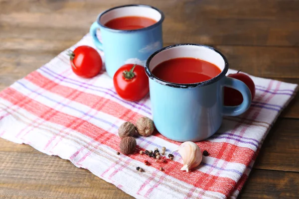 Sumo de tomate caseiro em canecas coloridas, especiarias e tomates frescos no guardanapo, no fundo de madeira — Fotografia de Stock