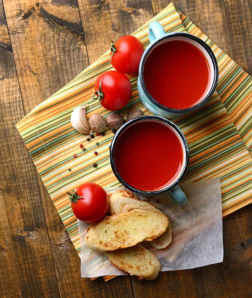 Homemade tomato juice in color mugs, toasts and fresh tomatoes on wooden background — Stock Photo, Image