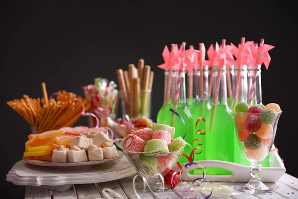 Bottles of drink with straw and sweets on dark background — Stock Photo, Image