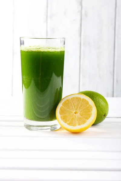 Lime juice and halves of lime and lemon on wooden table in front of wooden wall — Stock Photo, Image