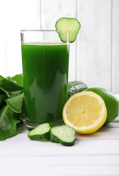 Lime juice, slices of cucumber halves of lime and lemon on wooden table in front of wooden wall — Stock Photo, Image