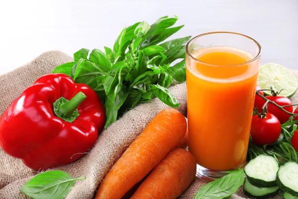 Glass of fresh carrot juice and vegetables on sacking napkin on wooden table — Stock Photo, Image