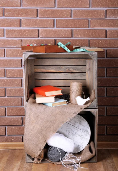 Sykit med tapeline, bøger, reb og legetøjsfugl på en trækasse foran murstensvæg - Stock-foto