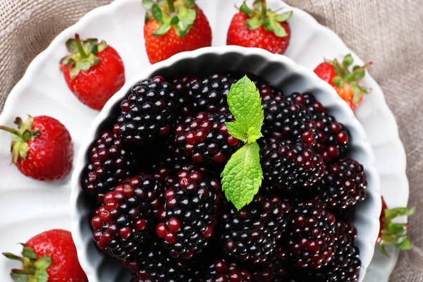 Bowl of blackberries and plate of strawberries on sacking background — Stock Photo, Image