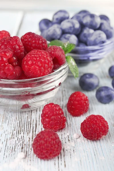 Glass bowls of raspberries and blueberries on wooden table on light background — Stock Photo, Image