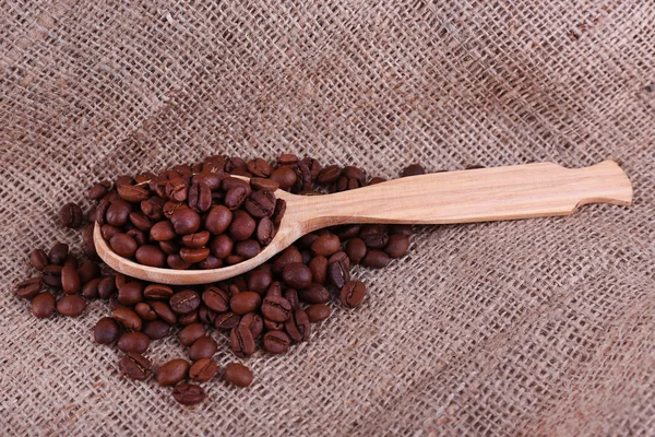 Cuchara de madera de granos de café sobre fondo de saqueo primer plano — Foto de Stock