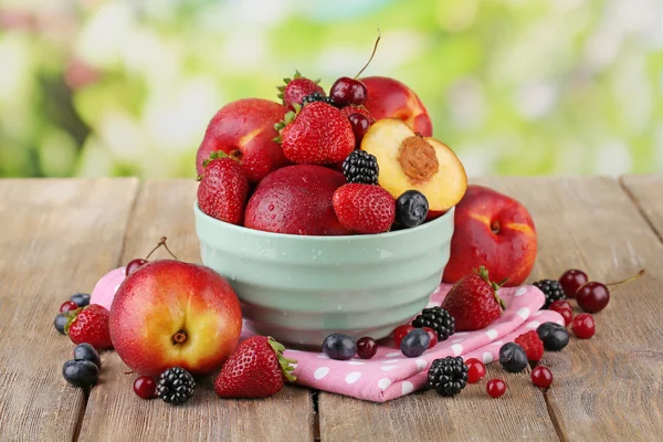 Brzoskwinie, jagody w misce na stole na naturalne tło — Zdjęcie stockowe
